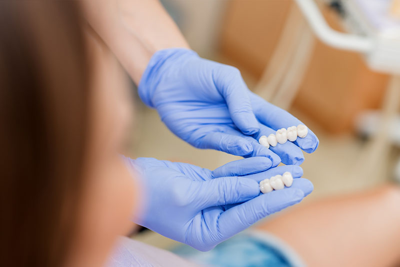 dentist holding veneers in front of patient with gloves on